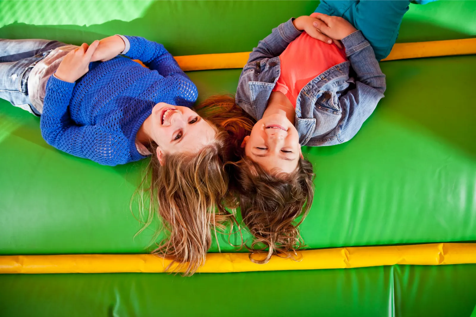 Three children lying back and laughing on the green floor of a bounce house.